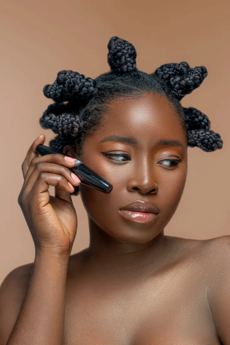 Beauty portrait with bantu knots holding a lip product against a warm backdrop