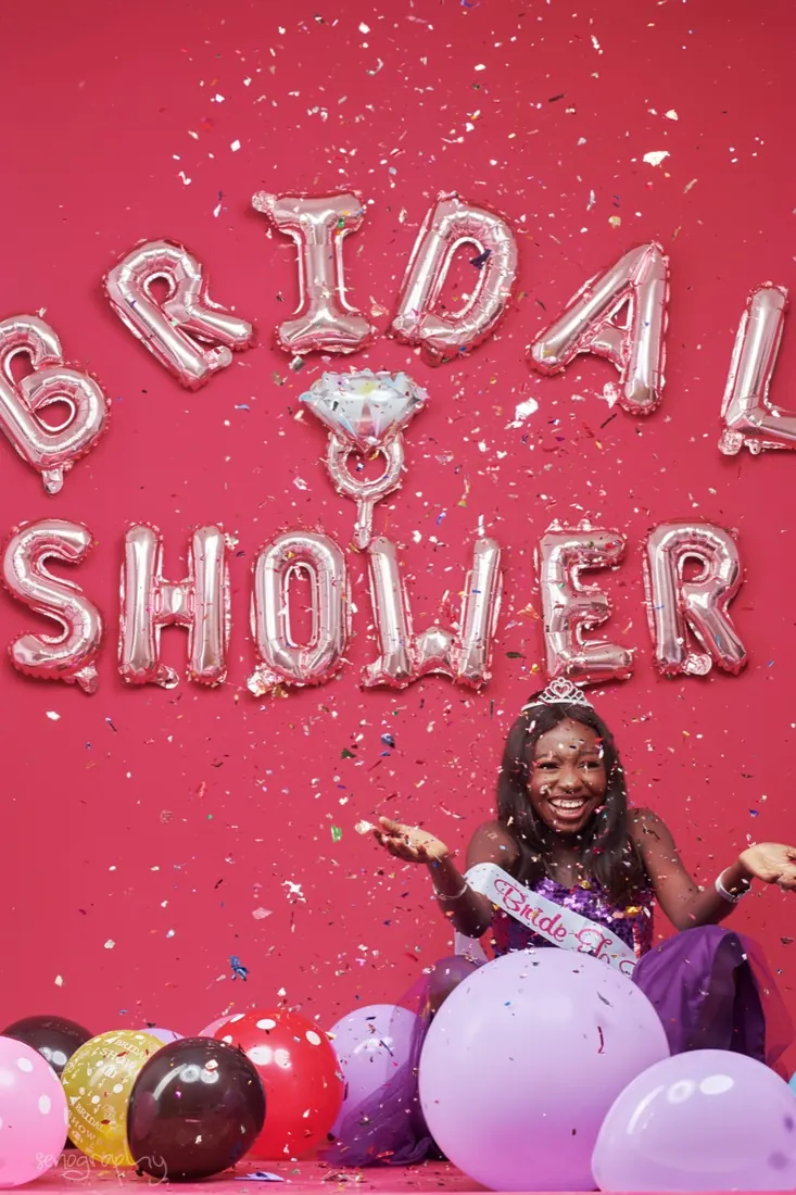 Bride-to-be throwing confetti beneath balloon lettering reading Bridal Shower