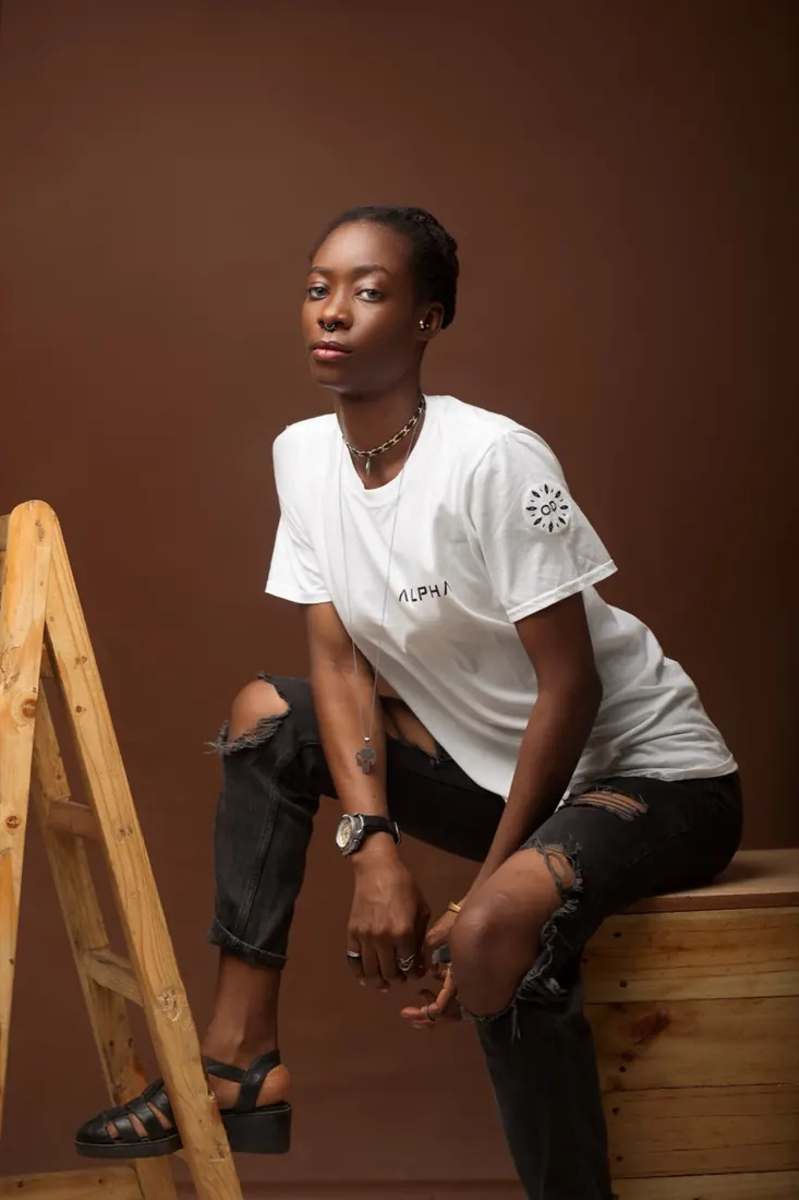 Seated portrait in a white tee and ripped jeans beside a wooden ladder